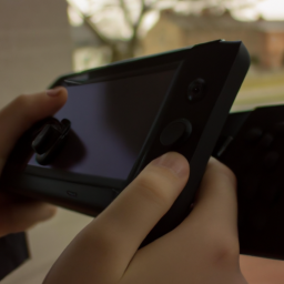 Description: A person holding a small, handheld device with a screen, buttons, and joysticks. The device is black and has a sleek, modern design.