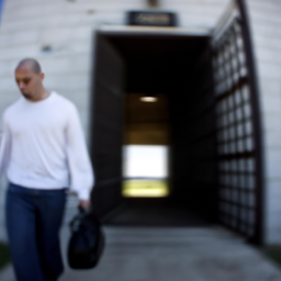 description: a blurred image of a man walking out of a prison gate, with a heavy bag on his shoulder and a somber expression on his face.