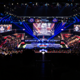 The image shows a packed stadium with fans from around the world, all cheering on their favorite teams in the LCK Spring Playoffs. The stage is set up with impressive lighting and production value, and the players are visible on stage, battling it out in intense matches. The energy in the stadium is palpable, with fans jumping up and down and waving their team's banners in the air.