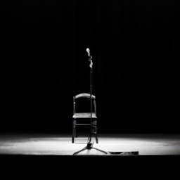 a black and white photograph of a stage with a microphone stand in the center, surrounded by empty seats. the stage lights are dimmed, casting a somber mood.